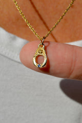 Gold necklace with a pendant featuring a blue and yellow gemstone held between fingers.