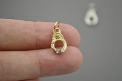 Gold pendant with a blue and yellow stone held between fingers against a neutral background
