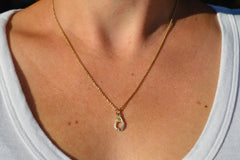 Gold necklace with a pendant on a person wearing a white tank top.