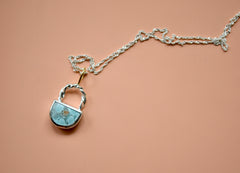 Light blue crescent shaped sand hill turquoise pendant with twisted wire and 18k gold bail. On orange background.