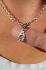 Silver necklace with a unique pendant held by a finger against a blurred background