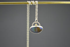 Unique boulder opal pendant that resembles a sandy beach  island with blue water and green line detail. Green gold dot detail on the top. On a silver chain.