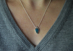 Necklace with a very colorful Australian boulder opal with blues and greens in it. Rose gold dot detail on top. On a silver chain. Shown worn on a model with gray sweater on