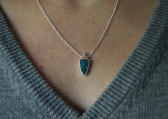 Necklace with a very colorful Australian boulder opal with blues and greens in it. Rose gold dot detail on top. On a silver chain. On model with gray sweater.