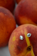 Silver ladybug stud earrings on a peach with other peaches in the background