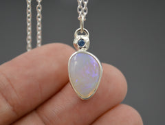 Pendant with an Australian Opal with a blue Montana sapphire set in a star on top of it. close up on fingertips