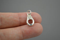 Silver pendant held between fingers against a gray background