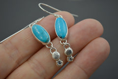 Sterling Silver Oval Turquoise dangle earrings with Montana sapphires set in stars on the bottom. Shown on hand.