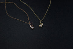 Two necklaces on a black background. Left is rose gold, right is yellow gold. They have tiny pendants with a star shape that contain a circular diamond.
