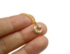 14k gold moon necklace, circular in shape with a crescent moon. Small faceted moonstone with a blue sheen in the top right of the circle.