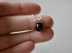 black onyx sphere hangs from a star encrusted pendant on a sterling silver chain. Held in a hand at the fingertips
