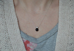 black onyx sphere hangs from a star encrusted pendant on a sterling silver chain. Being worn by a model with a cream sweater and gray/floral shirt.