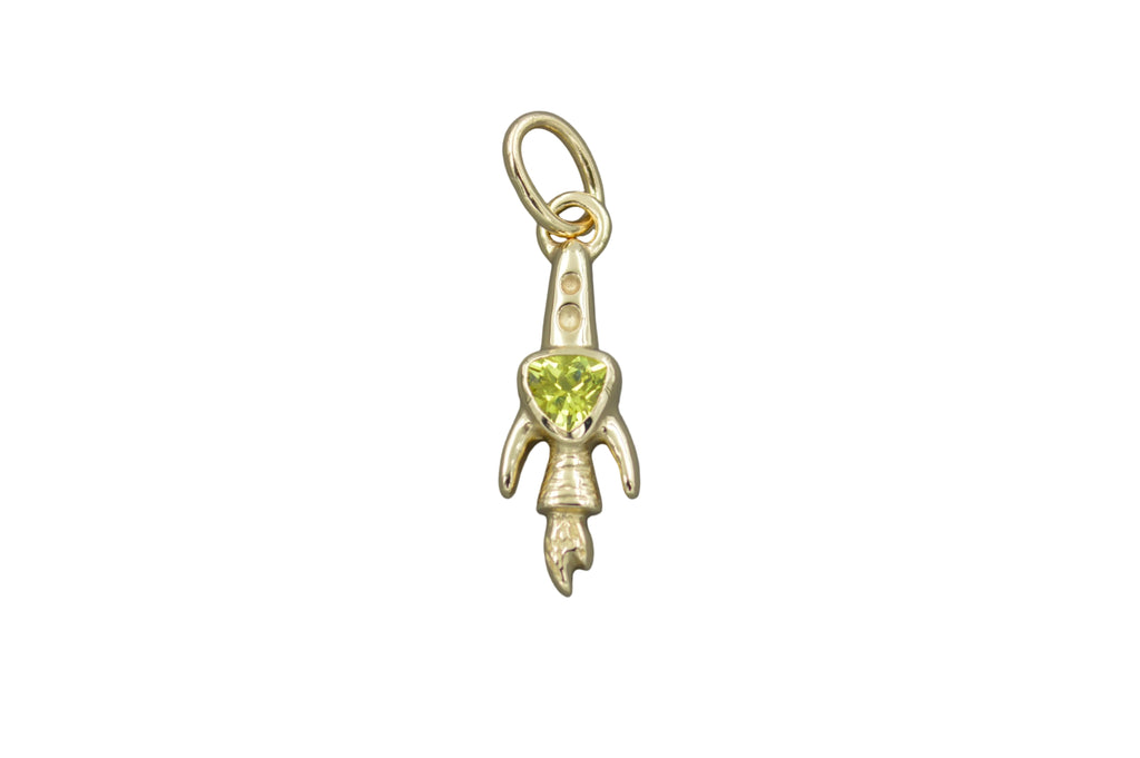 Gold rocket ship pendant with a green trillion gemstone on a gray background