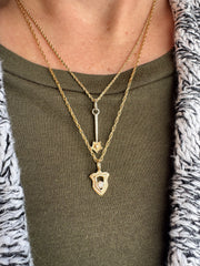 Close-up of a person wearing a gold necklace with a shield pendant and star wand pendant on a green shirt.