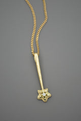 14k yellow gold star wand shaped pendant with a white diamond in the center of the star. Shown on a chain with a gray background.