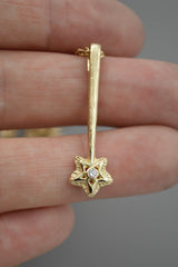14k yellow gold star wand shaped pendant with a white diamond in the center of the star. Resting on fingers.