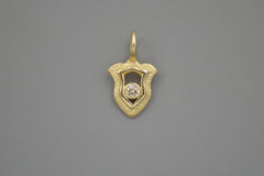 Gold shield pendant with a central champagne diamond on a gray background
