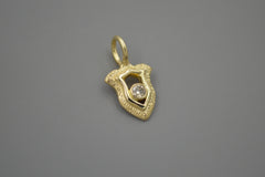 Gold shield pendant with a central champagne diamond on a gray background