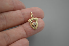 Gold shield pendant with a central champagne diamond held on fingers with a gray background.
