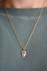 Gold necklace with a shield pendant with diamond on a green sweater