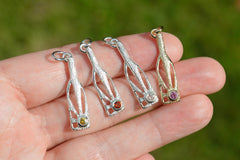 Three silver and one gold bottle-shaped pendants with sunshine rays within and gemstones on a hand against a blurred green background