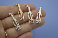Three silver and one gold bottle-shaped pendants with sunshine rays within and gemstones on a hand with blue background