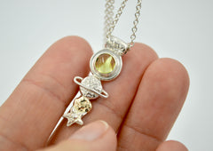 Celestial necklace with stars and planet shapes in silver and gold and a green peridot gemstone.