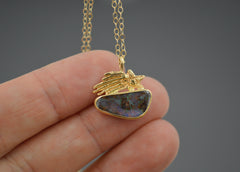 Gold pendant with a shooting star and Australian boulder opal resting on fingertips. Chain is seen above it