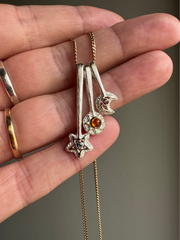 Wand pendants with different tops including a star, sun and moon as pendants. On a chain resting on a hand.