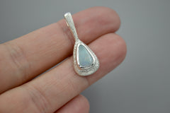 Teardrop-shaped wand pendant with a boulder opal gemstone on a gray background laying on fingertips