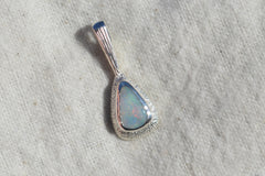 Opal pendant with silver setting on a textured beige background