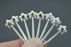 Silver and 14K Star Wand Pendants on a gray background each with a different colored gemstones held by fingertips