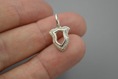 Silver shield pendant held between fingers against a neutral background