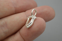 Silver shield pendant held between fingers against a neutral background