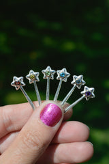 Star-shaped wand pendants with colored gemstones held by a hand against a blurred green background