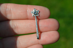 Silver star-shaped wand pendant held between fingers with a blurred green background