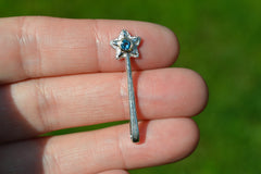 Small silver star-shaped wand pendant with a blue gemstone held between fingers against a green background
