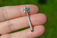 Small silver star-shaped wand pendant held between fingers with a green gemstone on a blurred green background