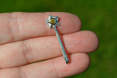 Small silver star-shaped wand pendant with a yellow gemstone held between fingers against a blurred green background