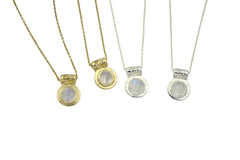 Four necklaces shown next to each other. From left to right, Gold tone necklace with rainbow moonstone, gold tone necklace with moonstone, silver necklace with rainbow moonstone, silver necklace with moonstone. Each necklace has a circular stone with tube shaped bail that has hand carved stars all around it.