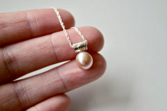Light Pink oblong pearl hangs from a star encrusted bail on a sterling silver chain, being held on a hand at the fingertips.