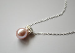 Light Pink oblong pearl hangs from a star encrusted bail on a sterling silver chain, on a light gray background