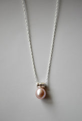 Light Pink oblong pearl hangs from a star encrusted bail on a sterling silver chain, on a gray background
